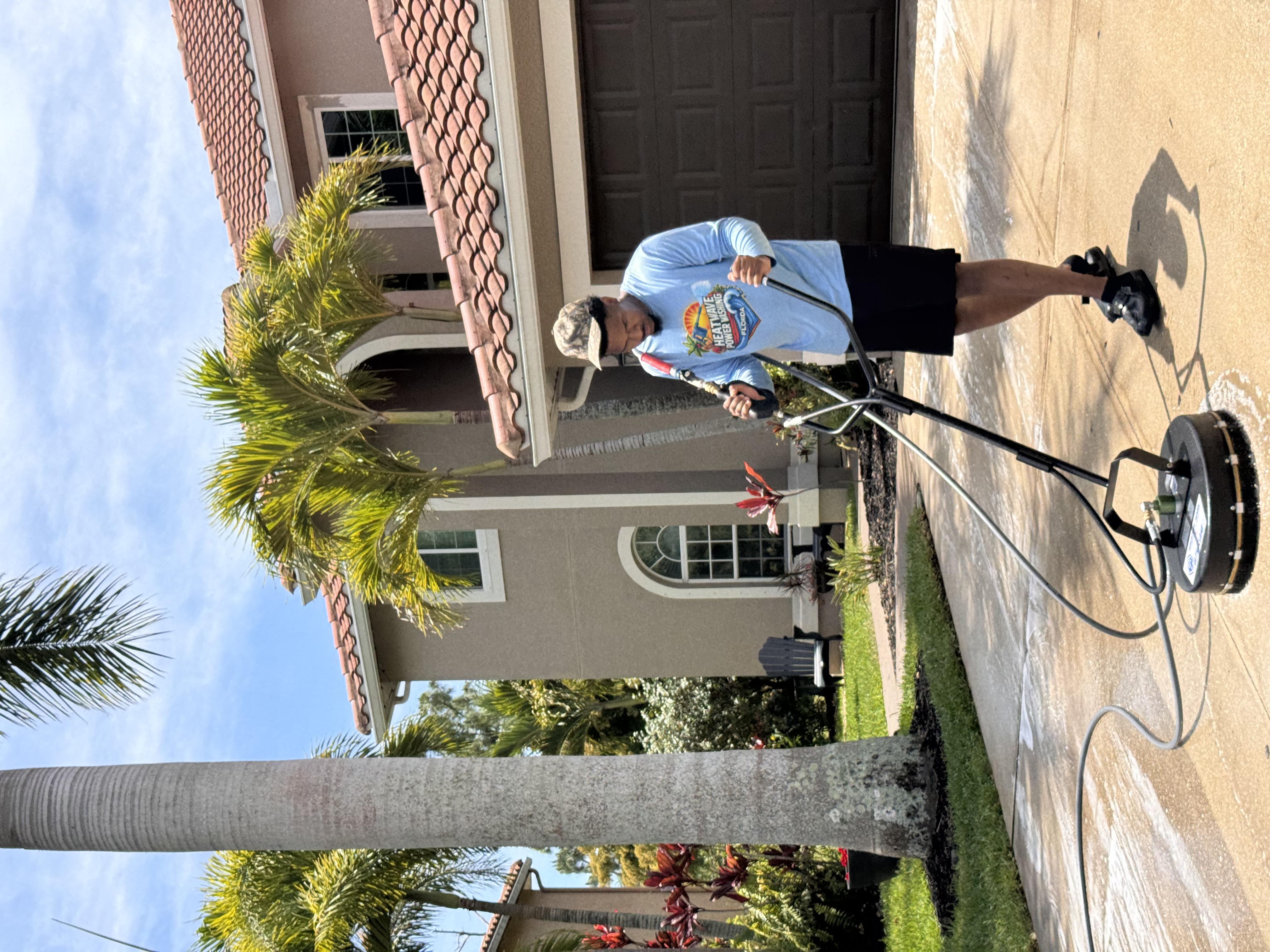 Technician cleaning a residential driveway with surface cleaner equipment.